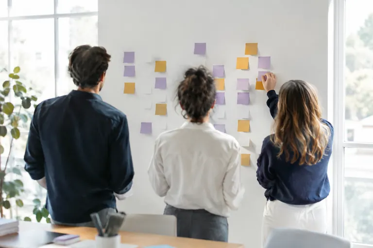 Équipe de dos devant un mur de notes colorées vierges pendant un atelier de travail