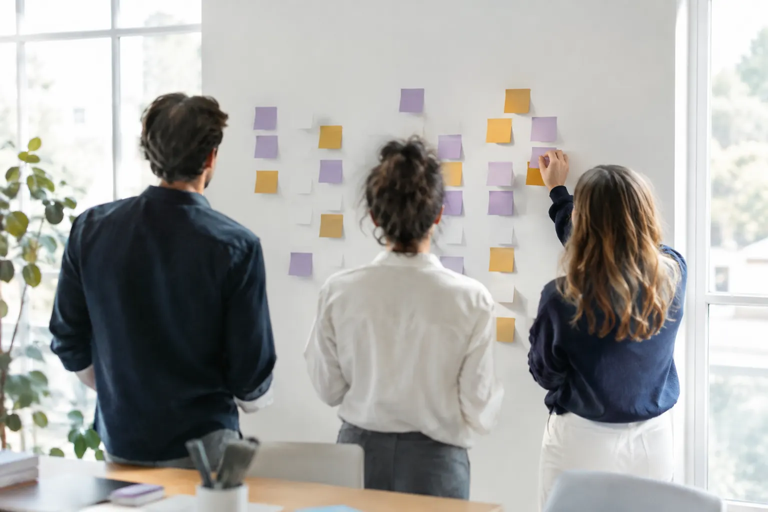 Équipe de dos devant un mur de notes colorées en atelier, illustration des soft skills du consultant SEO