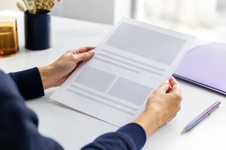 Mains tenant une feuille de CV vierge structurée au-dessus d'un bureau blanc